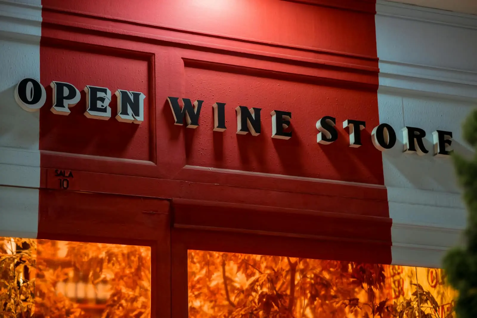 Letreiro Open Wine Store em letras em relevo sobre a fachada vermelha