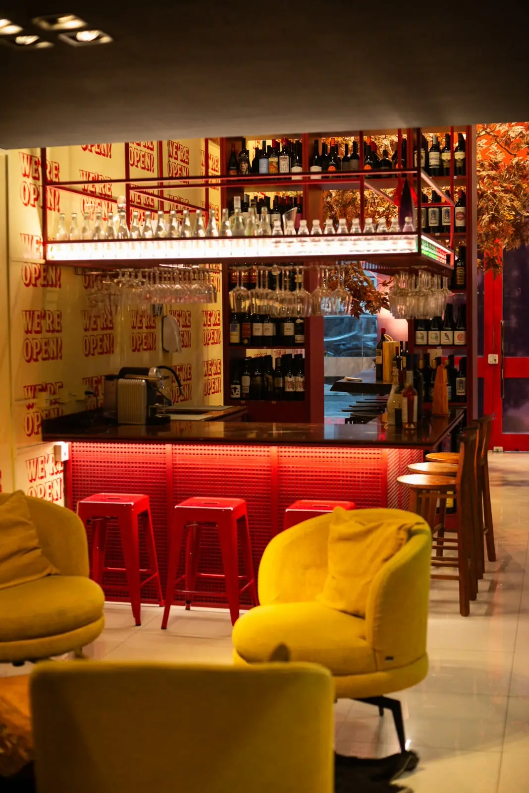 Poltronas amarelas em frente ao bar de banquetas vermelhas