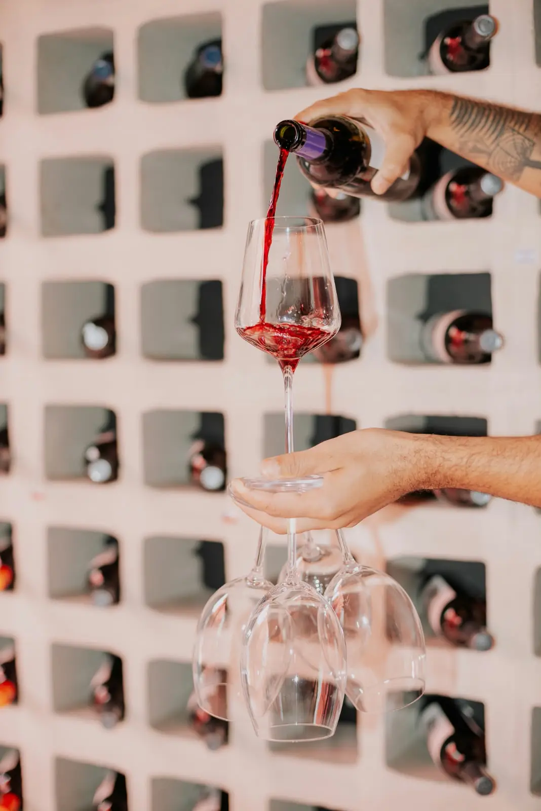 Vinho sendo servido em uma taça, com outras taças penduradas nos nichos