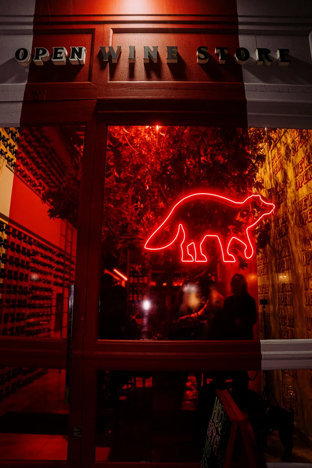 Vitrine à noite com o guaxinim de neon vermelho e folhagem ao fundo